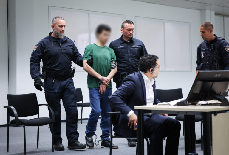 Wachmänner führen den Angeklagten Ibrahim A., im grünen T-Shirt und mit Handschellen, in den Gerichtssaal. Er hatte zwei Menschen in Brokstedt ermordet.