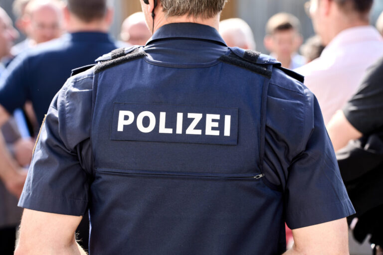 Es klingt wie ein furchtbares Verbrechen: Ein Mann soll seinen deutschen Schäferhund auf einen jungen Syrer gehetzt haben. Jetzt ermittelt die Polizei allerdings gegen den Ersteller der Anzeige. Denn der angebliche Angriff soll nie passiert sein. Ein Polizeiuniform steht vor einer Menschenmenge (Symbolbild). Hat einer von ihnen die Lüge verbreitet, ein Mann habe seinen Hund auf einen Syrer gehetzt?