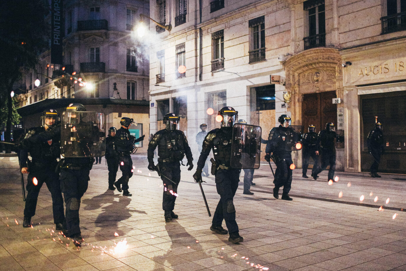 Französische Polizisten laufen in Lyon eine Straße entlang, während Feuerwerkskörper und Tränengas vorbei fliegen. Nach den Parlamentswahlen kam es im ganzen Land zu Ausschreitungen.