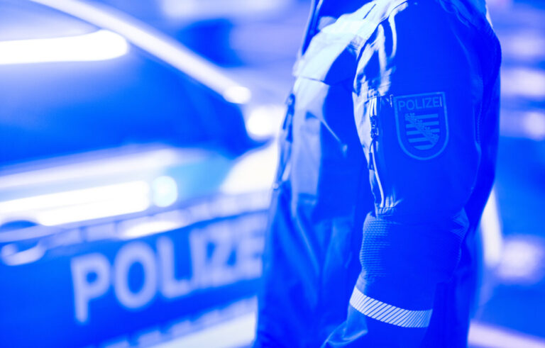 Ein Polizist steht neben einem Polizeiauto. Es gibt neue Zahlen zur Kriminalität von Ausländern in Sachsen.