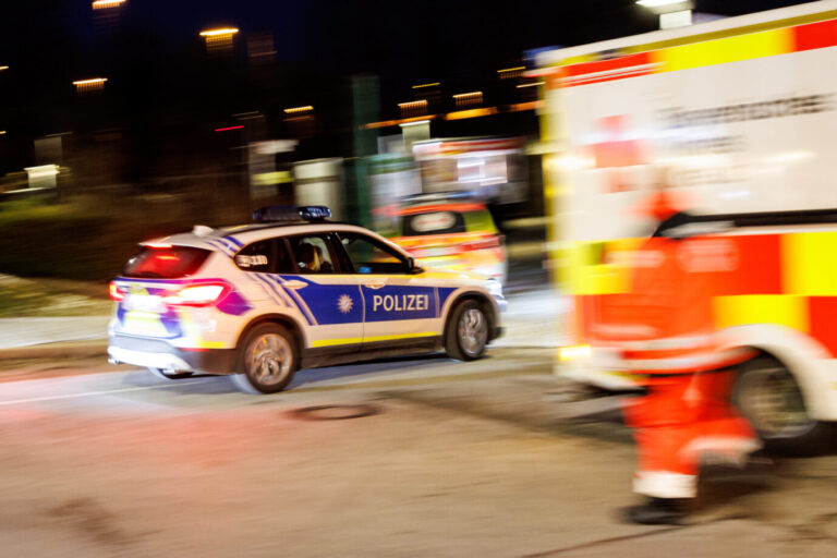 Ein Einsatzfahrzeug der Polizei kommt zur Unterstützung zu einem während eines Rettungseinsatzes an einem Einsatzort geparkten Rettungswagen vom Bayerischen Roten Kreuz. Das Sicherheitsgefühl in Deutschland sinkt. (Aufnahme mit langer Verschlusszeit)