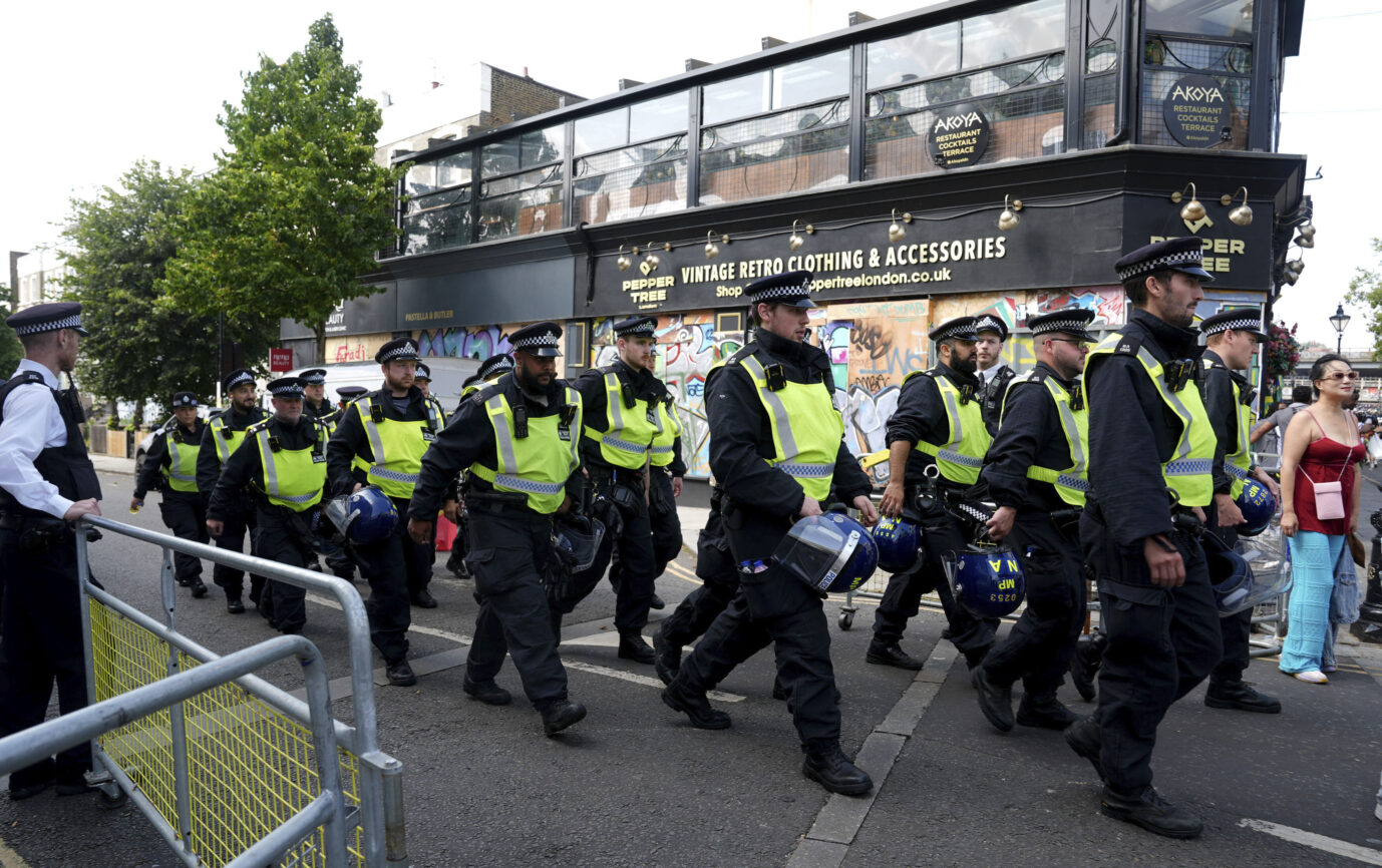 Während des Notting Hill Karneval laufen Polizisten in gelben Warnjacken eine Straße. in London entlang