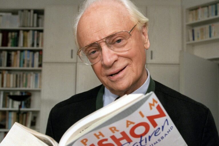 Ephraim Kishon hält in den Räumen seines Münchener Hausverlags eines seiner eigenen Bücher in die Kamera und lächelt, 1999