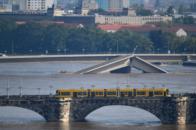 Die Hochwasser führende Elbe fließt an der teileingestürzten Carolabrücke entlang, im Vordergrund fährt eine Straßenbahn der Dresdner Verkehrsbetriebe (DVB) über die Augustusbrücke. Der Pegelstand der Elbe in Dresden beträgt momentan 6,05 Meter.