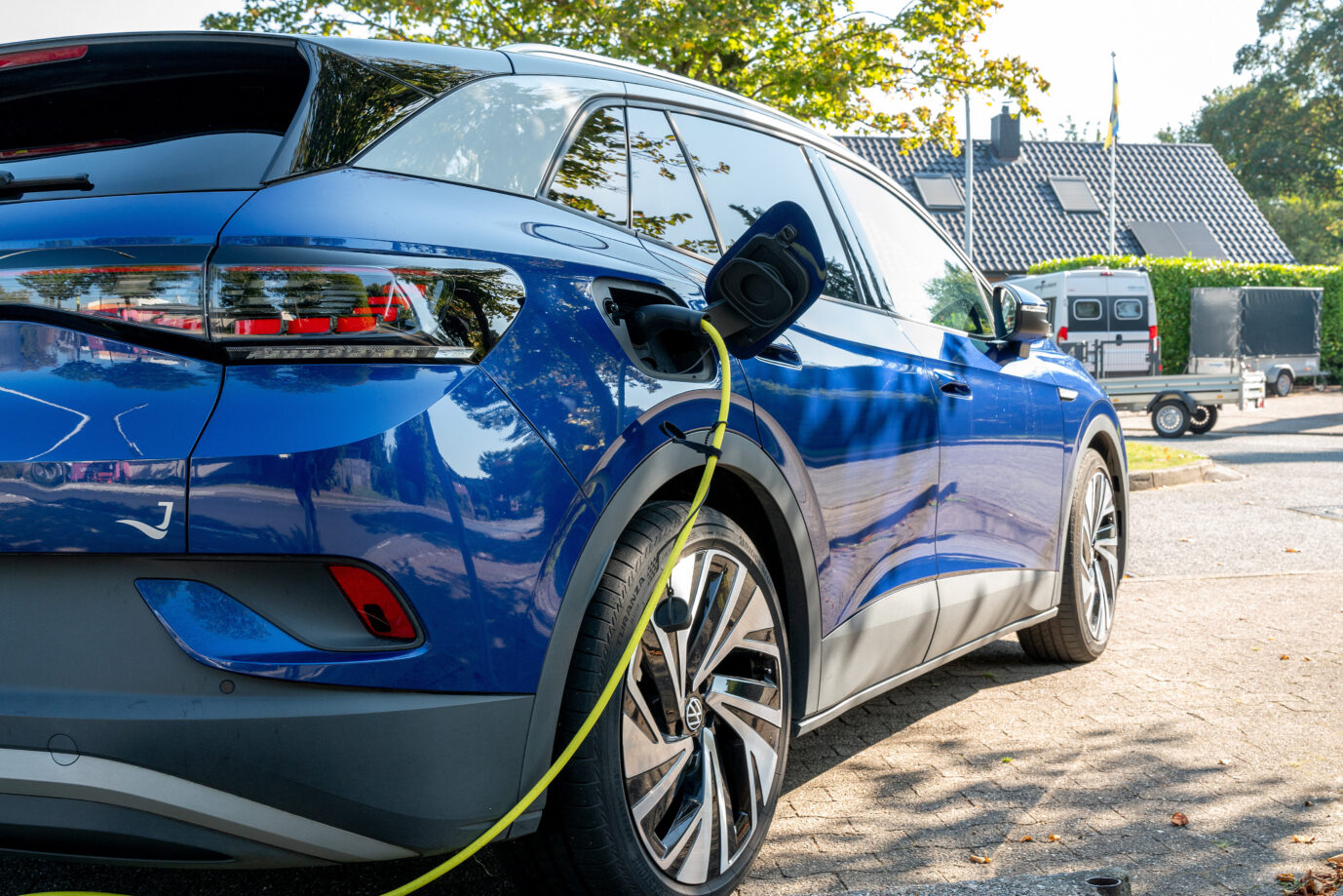 Ein blaues E-Auto von Volkswagen steht neben einer Ladestation, ein gelbes Ladekabel ragt aus dem Fahrzeug und aus dem Bild heraus