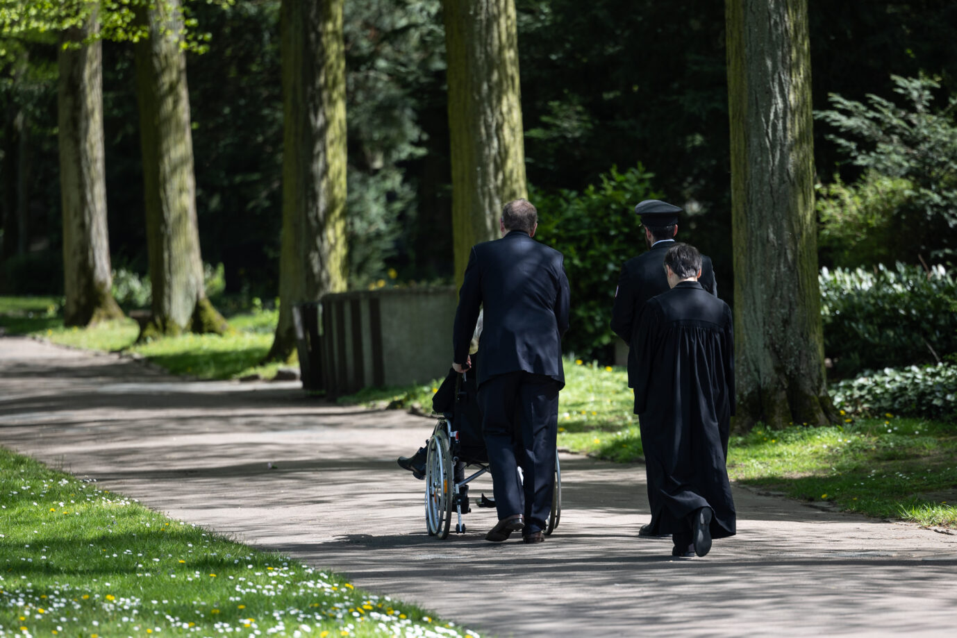 Schwarz gekleidete Personen laufen einen Pfad an einem Friedhof entlang – eine Trauergemeinde. Ob sie das geerbte Geld wohl behalten dürfen? Oder wird ihnen die Erbschaftssteuer einen Strich durch die Rechnung zu machen?