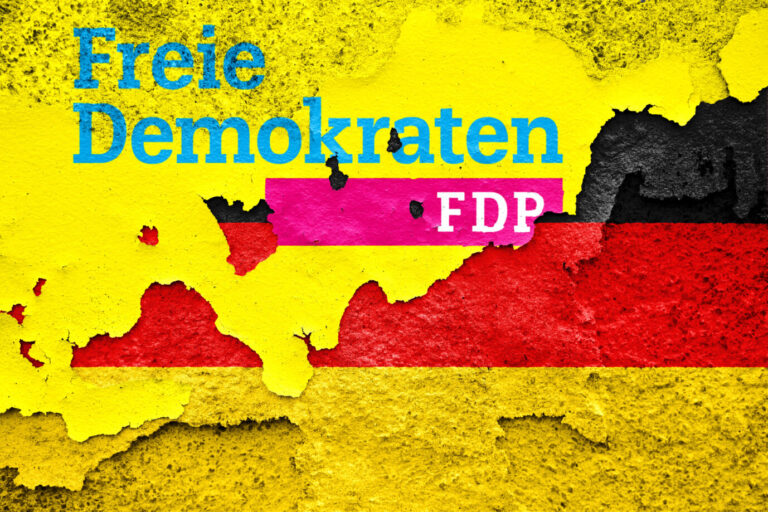 Gelber, mit einem FDP-Logo versehener, Lack blättert von einer Deutschlandfahne ab