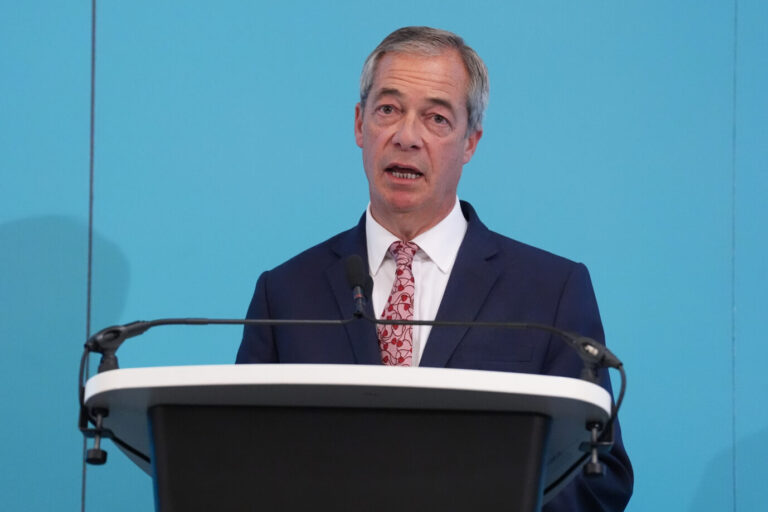 Der Vorsitzende von „Reform UK“, Nigel Farage, steht vor einem Rednerpulzt und spricht mit leidendem Gesichtsausdruck ins Mikrofon. Dazu trägt er einen schwarzen Anzug mit rosa Krawatte. Aufgrund eines erneuten Messermords durch einen Migranten, kritisiert Farage die Regierung