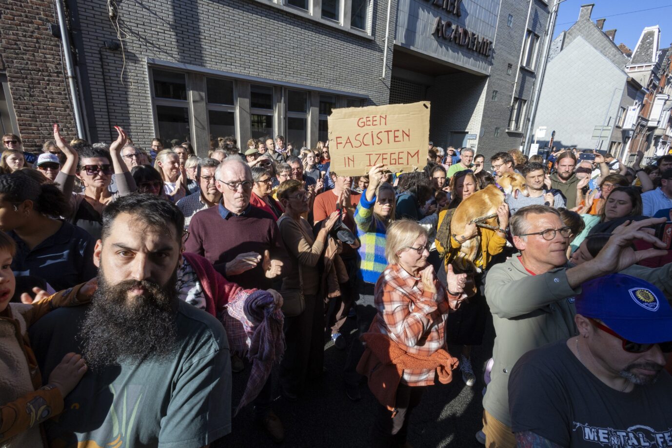 Eine Menschenmasse ist im belgischen Izegem zu sehen, einige von ihnen halten Schilder hoch auf denen "Gegen Faschisten in Izegem" steht.