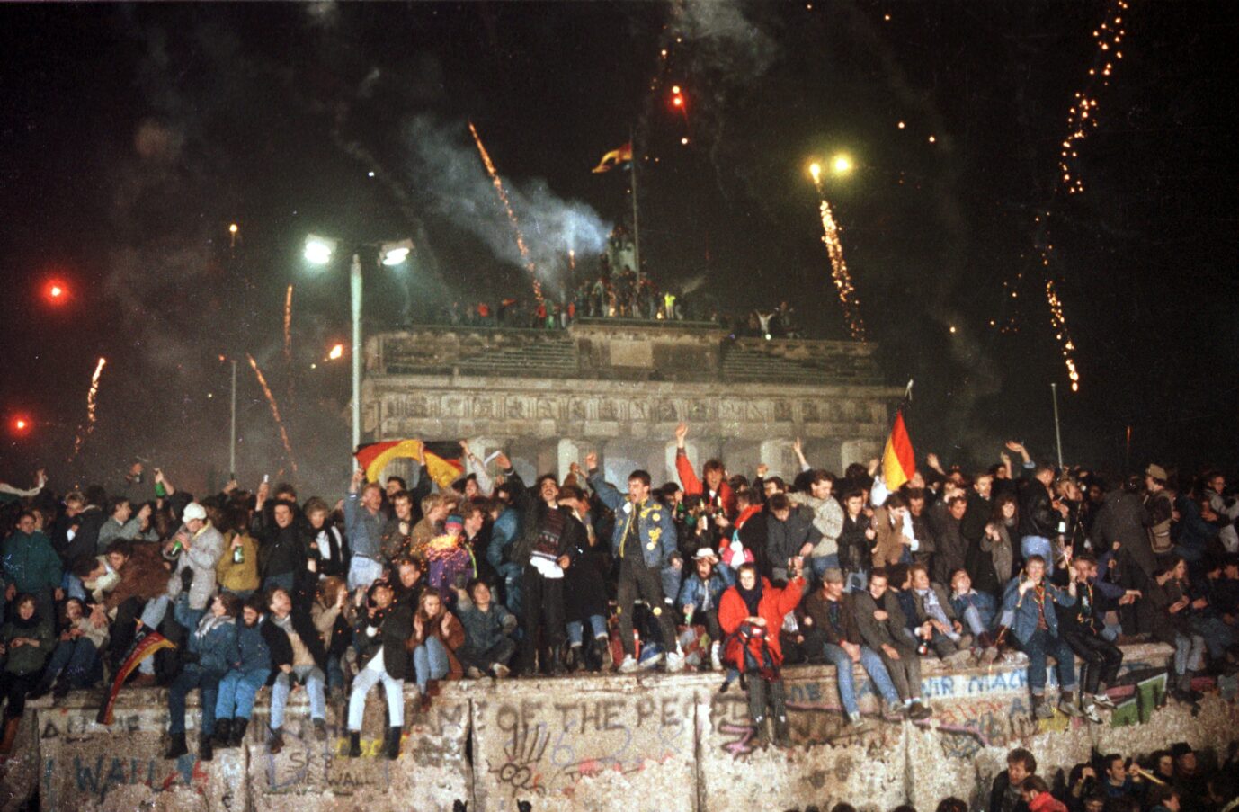 Ausgelassen feiern die Berliner am 31.12.1989 auf der Berliner Mauer vor dem Brandenburger Tor. Zur ersten deutsch-deutschen Silvesterfeier waren mehrere hunderttausend Menschen aus Ost und West gekommen. Der Untergang des SED-Regimes hatte sich 1989 in einem rasanten Tempo vollzogen: Unter dem Druck der Bevölkerung öffnete die DDR am 9.11.1989 ihre Grenzen.