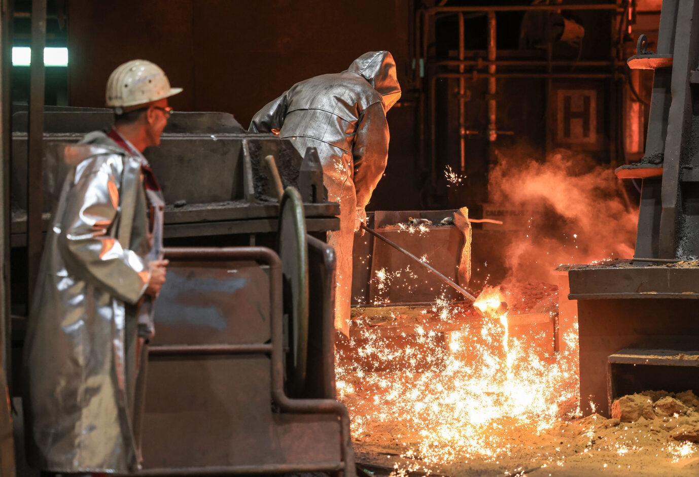 Zwei Männer in silber glänzenden Schutzanzügen gießen im Stahlwerk von ThyssenKrupp irgendetwas Feuriges und Funkensprühendes um. Das Werk soll an eine indisch-japanische Firma verkauft werden