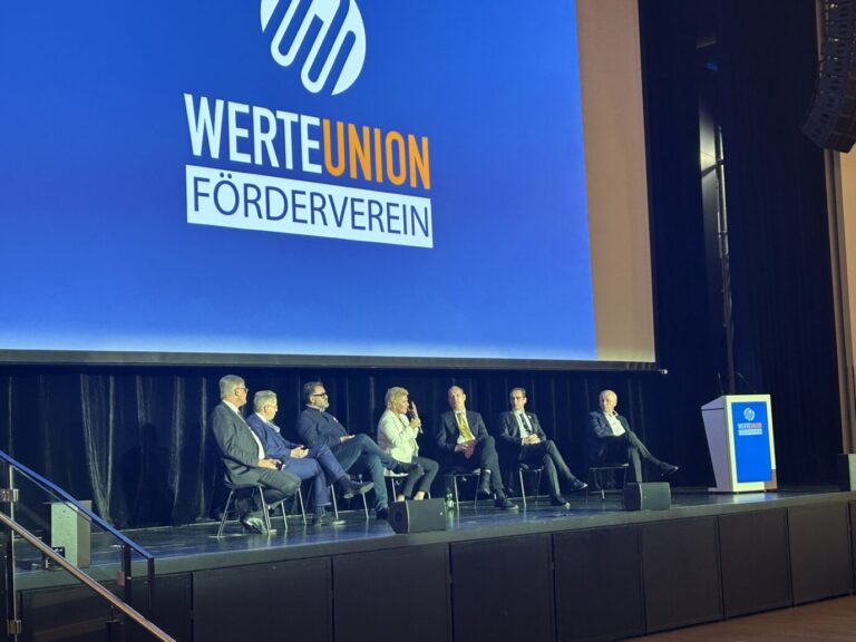 Auf einer Bühne über der riesig groß das Logo der WerteUnion zu sehen ist, sitzen: WU-Mitglied Jörg Meuthen, WU-Vorsitzender Hans-Georg Maaßen, Buchautor Tom Lausen, WU-Politikerin Sylvia Pantel, Filmemacher Jimmy Gerum, WU-Vorsitzender in Rheinland-Pfalz, Eugen Radtke und Michael Buback. Jan Böhmermann war nicht vor Ort