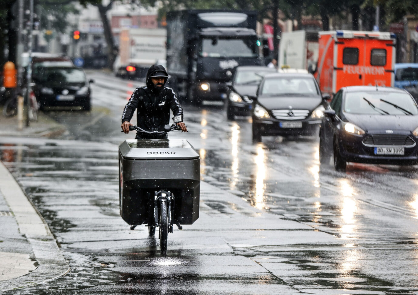 Berlin, 20.06.2023 - Ein Mann fahert bei starkem Regen mit einem Lastenrad ueber eine regenasse Straase.