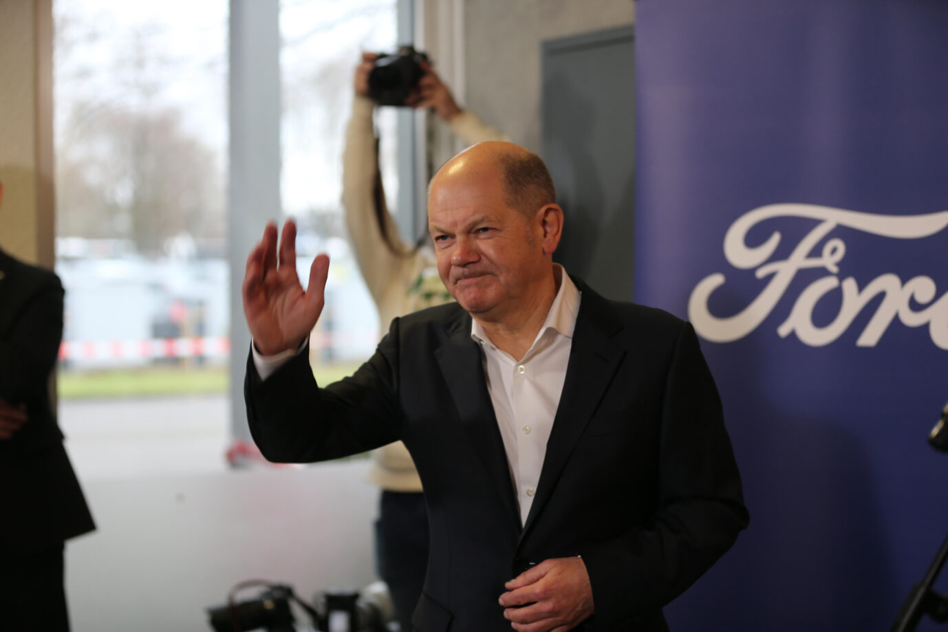 Bundeskanzler Olaf Scholz (SPD) hebt während einer Rede im Kölner Ford-Werk die Hand und macht eine grimmige Grimasse. Am Dienstag forderte er die Wiedereinführung der E-Auto-Prämie