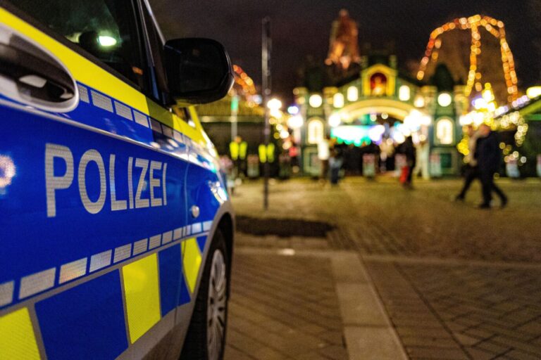 Das Bild zeigt einen Polizeiwagen bei einem Weihnachtsmarkt.