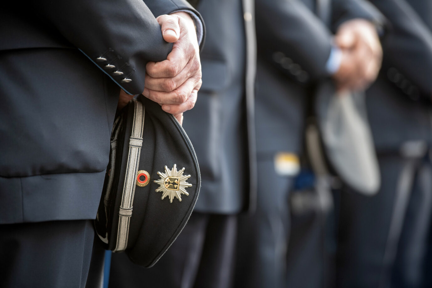 Beamte der Bundespolizei halten bei einer Vereidigungsfeier im Innenhof der Bundespolizeiinspektion am Flughafen Frankfurt ihre Mützen in der Hand. Die Vereidigung bildet das offizielle Ende der Ausbildung, nach der die Beamten in den Regeldienst wechseln. Bundespolizisten halten zur Vereidigung ihre Mützen in der Hand: Wer sie unterrichten darf, wird hart umkämpft. Foto: picture alliance/dpa | Boris Roessler