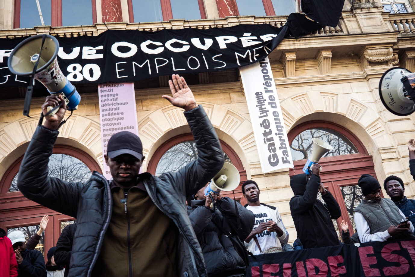 Vor dem linken Pariser Theater Migrantische Demonstranten stehen vor dem linken Theater „Gaîté Lyrique“ steht ein afrikanischer MIgrant, reckt ein Megaphon in die Höhe und demonstriert. Seit Dezember halten er und andere Migranten das Gebäude besetzt