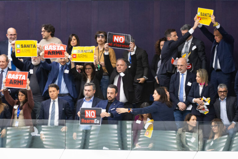 Das Bild zeigt Besucher im EU-Parlament, die mit Schildern gegen „Rearm Europe“ protestieren.