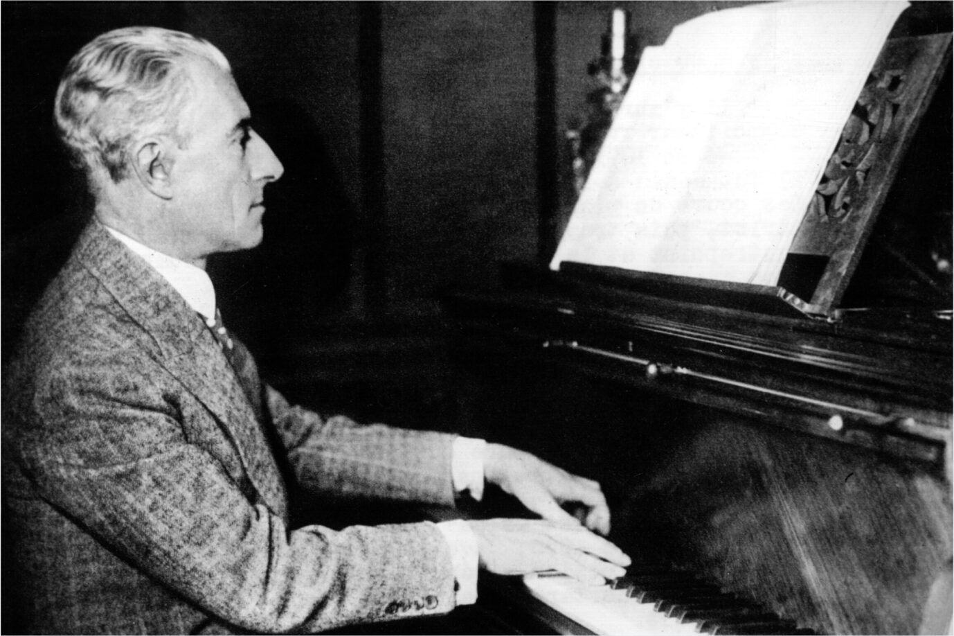 Der französische Komponist Maurice Ravel sitzt in einem alten schwarzweiß-Foto an einem Klavier und spielt es