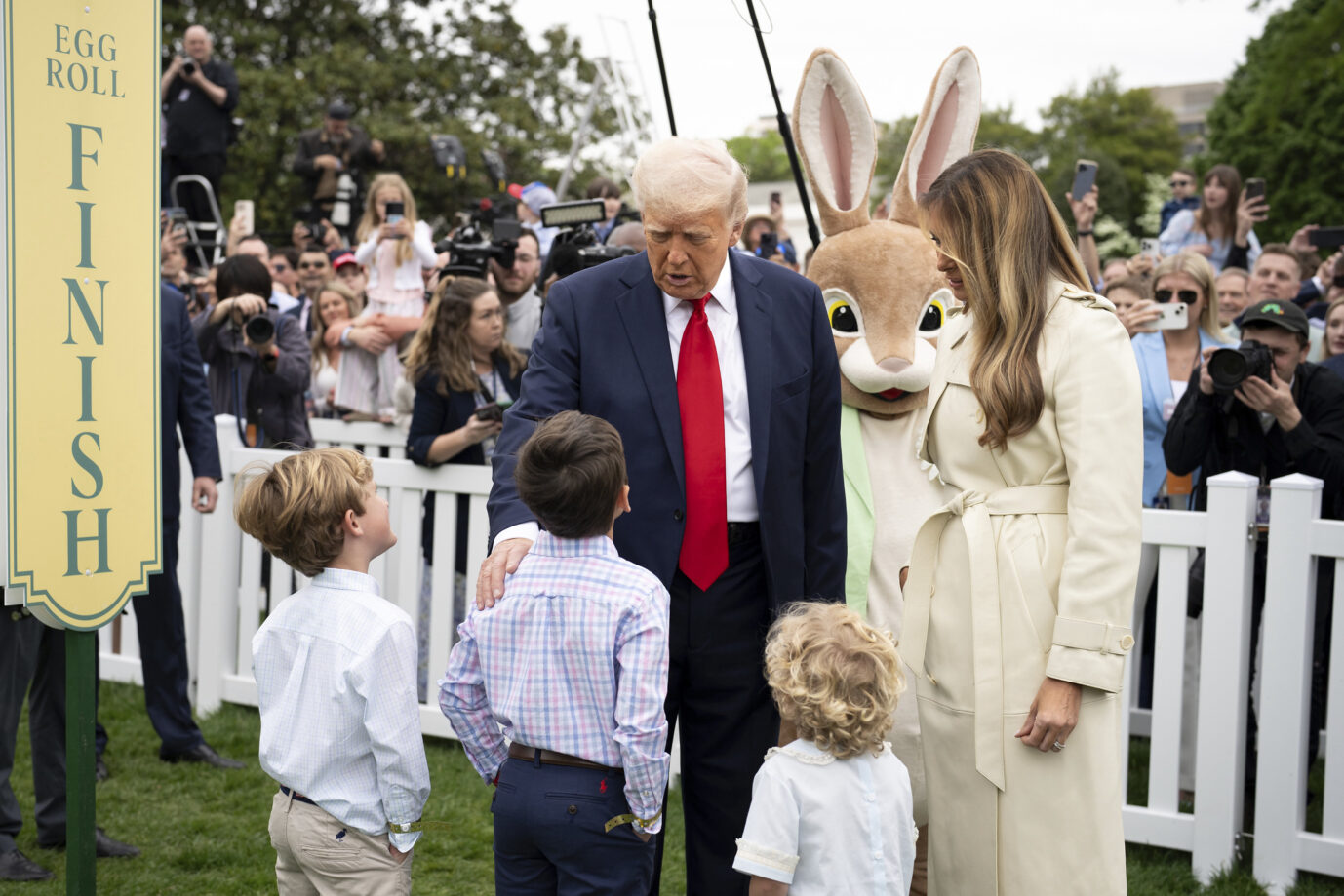US-Präsident Donald Trump und seine Ehefrau Melania Trump stehen auf dem Rasen vor dem Weißen Haus und sprechen mit einigen Kindern – im Hintergrund ist ein Osterhase zu sehen – ein Symbol für Fruchtbarkeit und die Geburtenrate der USA