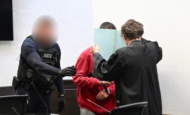 Der Afghane wird vor Prozeßbeginn mit einem Aktendeckel vor dem Gesicht in den Gerichtssaal geführt. Foto: picture alliance/dpa | Bernd Weißbrod
