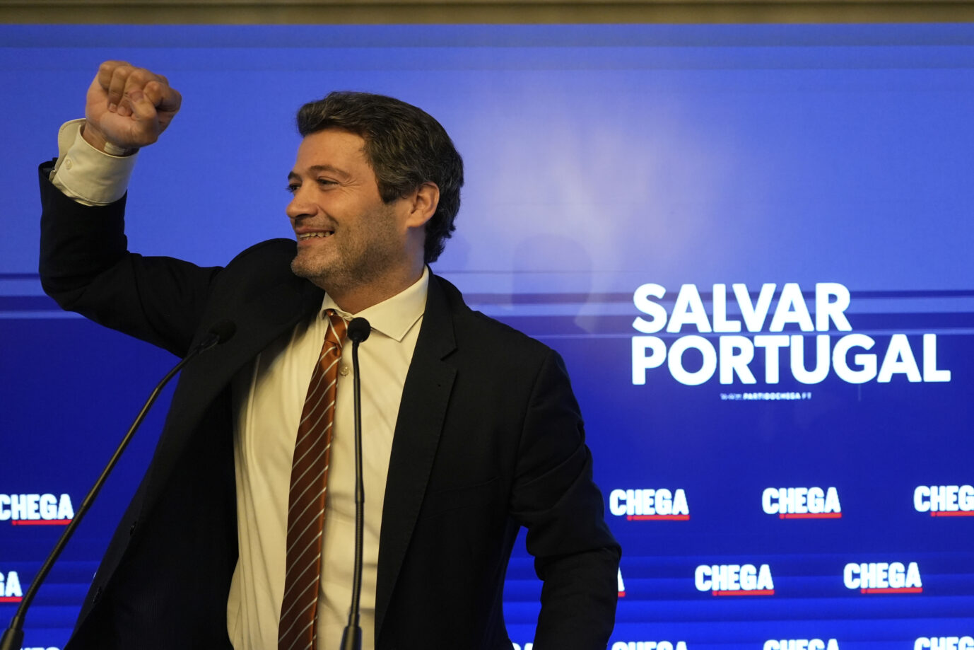 Der Vorsitzende der portugiesischen Chega-Partei, André Ventura, steht vor einem blauen Hintergrund und hebt seine Faust triumphierend in die Höhe – Symbolisch stehend für den phänomenalen Wahlerfolg, den die rechtskonservative Partei am Sonntag hingelegt hat