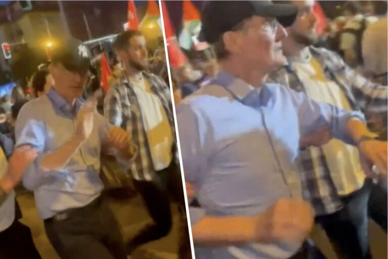 Gesundheitsminister Karl Lauterbach (SPD) trägt ein himmelblaues Hemd und eine schwarze Baseballcap, er hebt abwehrend die Hände in Richtung der aggressiven 1. Mai-Demonstranten, die ihn beschimpfen