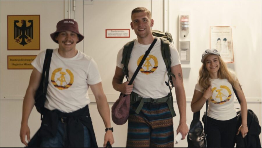 Zwei junge Männer und eine junge Frau stehen nebeinander und lächeln, dabei tragen sie Shirts mit einem Aufdruck des DDR-Logos – es handelt sich um Anhänger der Identitären Bewegung, die wegen des Verstoßes gegen ein Ausreiseverbot verhaftet wurden