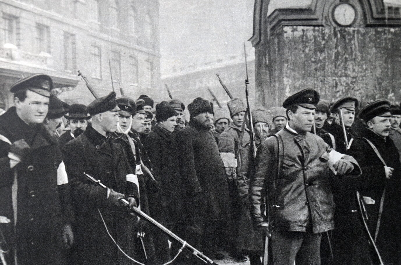 Auf einem alten schwarz-weiß-Foto sind bwaffnete revoltierende Soldaten und Bürger zu sehen, die grimmig gucken und auf einer Straße in Sankt Petersburg (damals Petrograd) stehen – während der Februarrevolution 1917, als der Zar gestürzt wurde