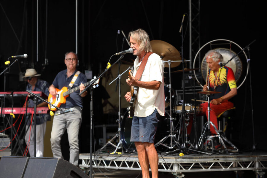 Die bekannte Krautrock-Band Guru Guru während eines Konzerts – man sieht alte Männer in Hippie-artigen Klamotten die Gitarre und Schlagzeug spielen