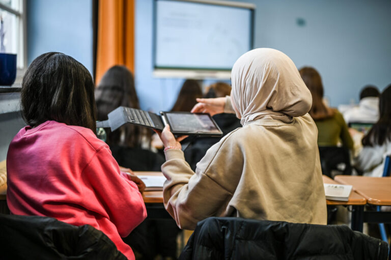Zwei offenbar migrantische oder muslimische Schülerinnen – eine mit dunklen Haaren, eine mit Kopftuch – sitzen in einem Klassenraum – Symbolbild dafür, daß ein homosexueller Lehrer in Berlin aufgrund seiner Sexualität gemobbt wird
