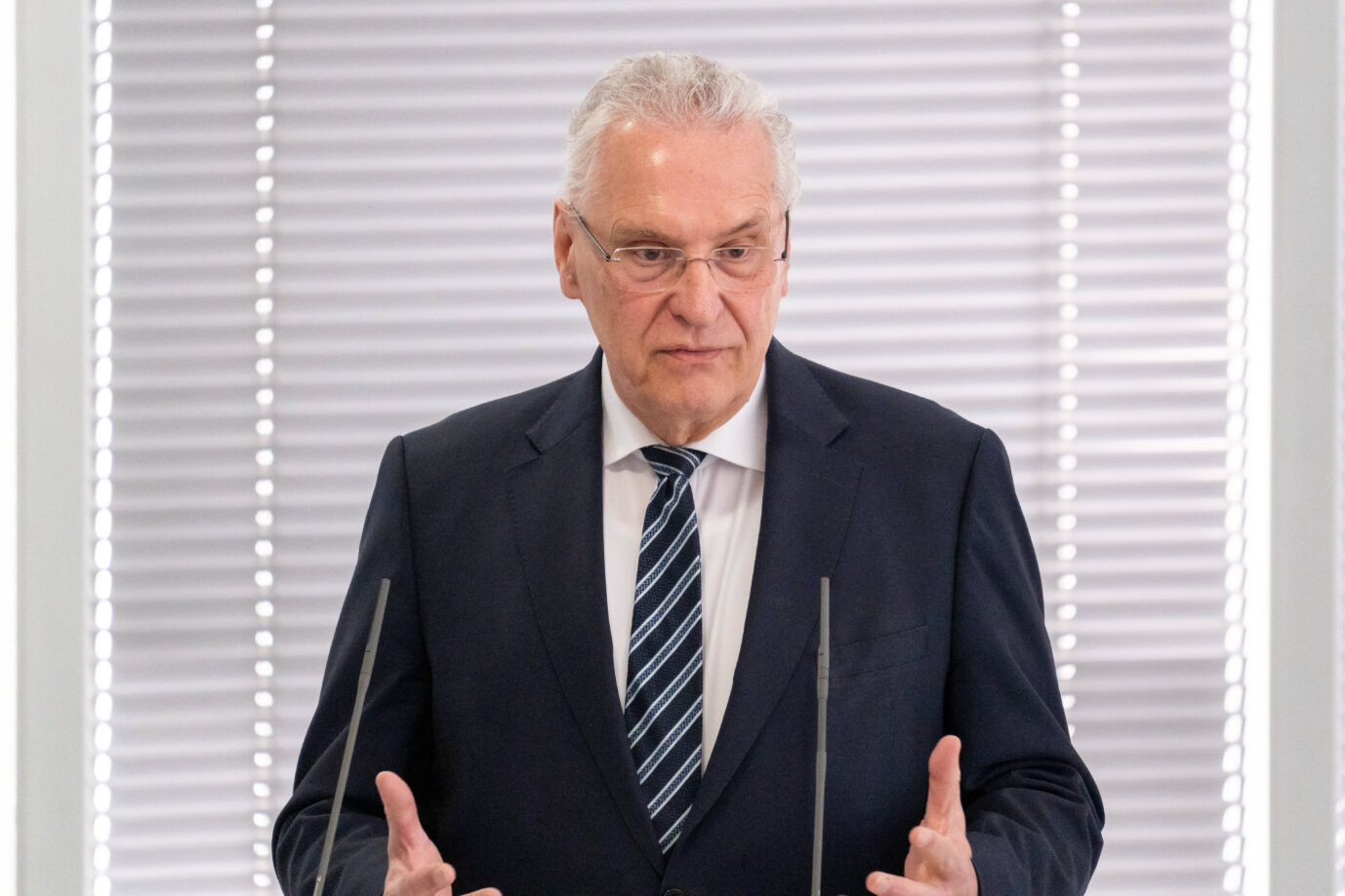 Bayerns Innen- und Integrationsminister Joachim Herrmann (CSU) steht mit einem schwarzen Jackett da und gestikuliert mit seinen Händen – heute äußerte er Lob und Sorge über die Zahl der Einbürgerungen