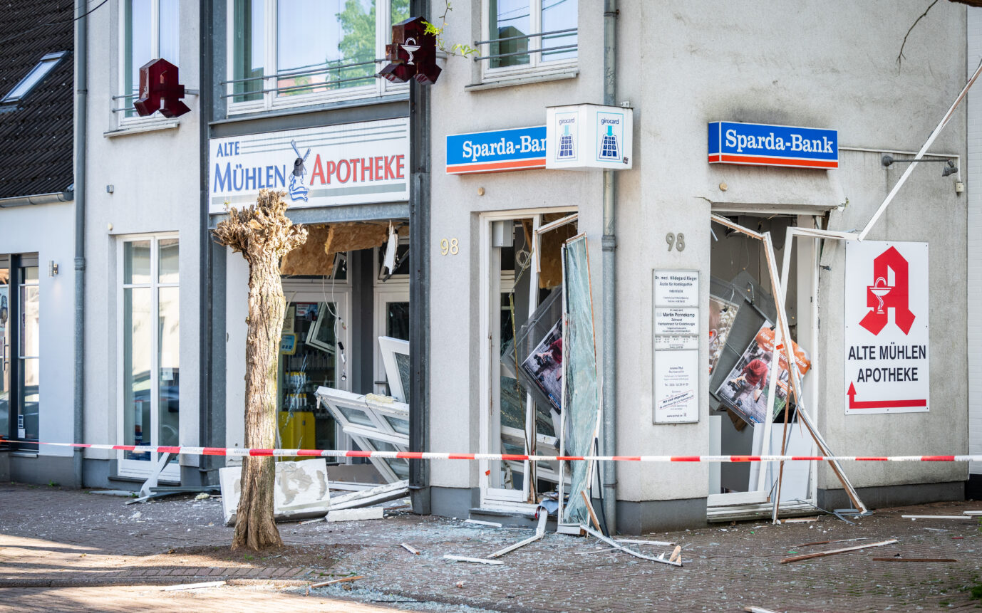 Zerstörte Filiale der Sparda-Bank an der Düsseldorfer Straße in Mülheim an der Ruhr nach einer Geldautomatensprengung. Die Glasfassade ist vollständig herausgerissen, Trümmer und Splitter liegen auf dem Gehweg. Auch das benachbarte Gebäude mit einer Apotheke ist betroffen. Der Bereich ist mit rot-weißem Flatterband abgesperrt. Die Tat ereignete sich in der Nacht zum 26. April 2025 im Stadtteil Altes Dorf Saarn.
