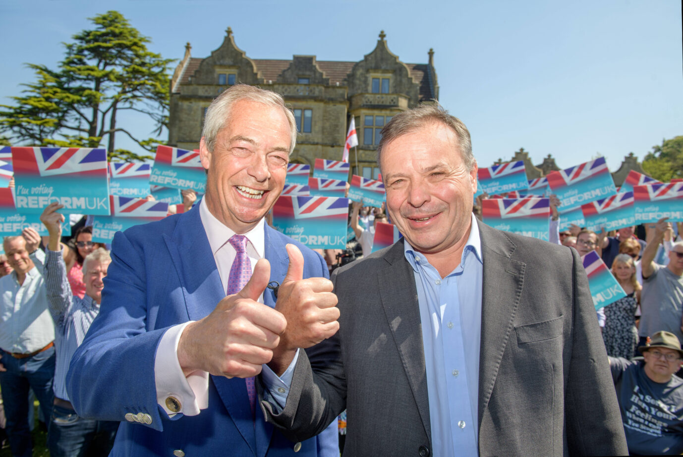 Links steht der Chef der Reform UK-Partei, Nigel Farage und macht die "Daumen hoch"-Geste, rechts neben ihm steht der Parteikandidat für Westengland, Arron Banks und macht ebenfalls "Daumen hoch"