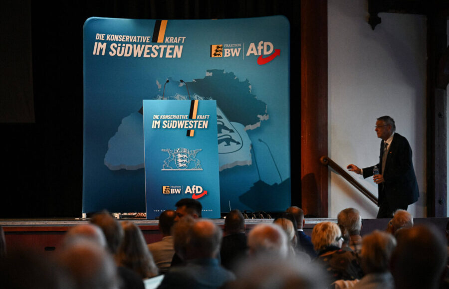 Auf einer spärlich beleuchteten Bühne ist das Logo des AfD-Landesverbands Baden-Württemberg zu sehen, rechts betritt der der Landtagsabgeordnete Hans-Peter Hörner die Bühne – Symbolbild dafür, wie der Verfassungsschutz die verschiedenen Landesverbände einstuft