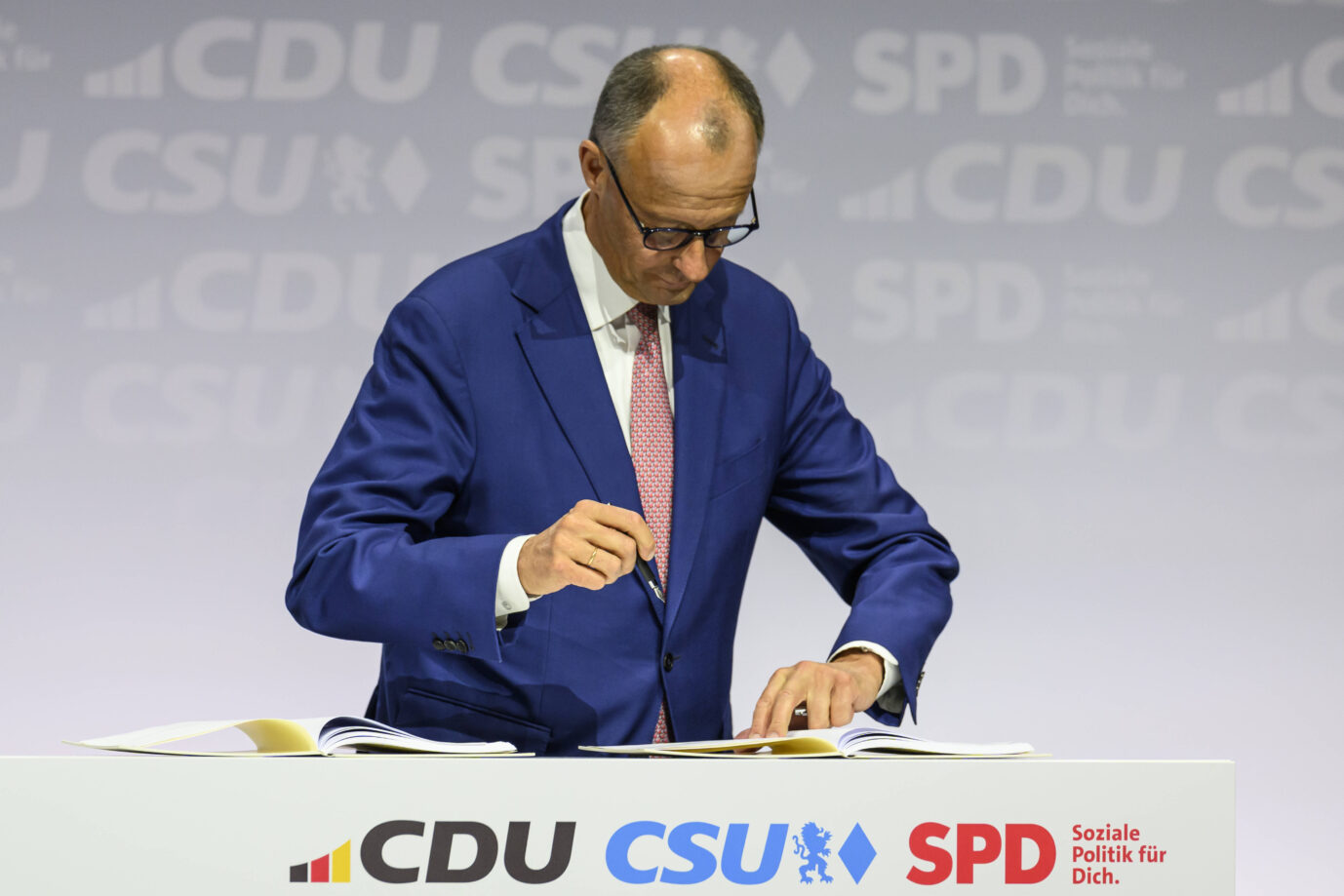 Unions-Chef Friedrich Merz steht vor einem Pult und unterzeichnet mit einem Füllfederhalter ein Dokument – Symbolbild dafür, daß die mutmaßliche neue Regierung in einem Beschlußpapier die Streichung von insgesamt 25 Beauftragten plant