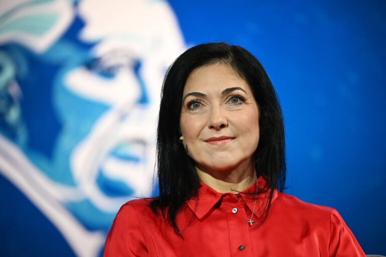 Katherina Reiche, die neue Bundeswirtschaftsministerin, steht in einer leuchtend roten Bluse vor einem großflächigen, stilisierten Hintergrundbild von Ludwig Erhard in Blautönen. Im Fokus des Fotos ist ihr Gesicht, sie blickt mit leichtem Lächeln und ruhigem Ausdruck in die Kamera. Reiche trägt ein dezentes Mikrofon am rechten Ohr und eine feine Halskette mit einem kleinen Kreuzanhänger. Die Aufnahme entstand beim Ludwig-Erhard-Gipfel am Tegernsee, wo sie ihren wirtschaftspolitischen Vier-Punkte-Plan präsentierte. Wirtschaftsministerin Katherina Reiche beim Ludwig-Erhard-Gipfel am Tegernsee. Foto: IMAGO / Sven Simon