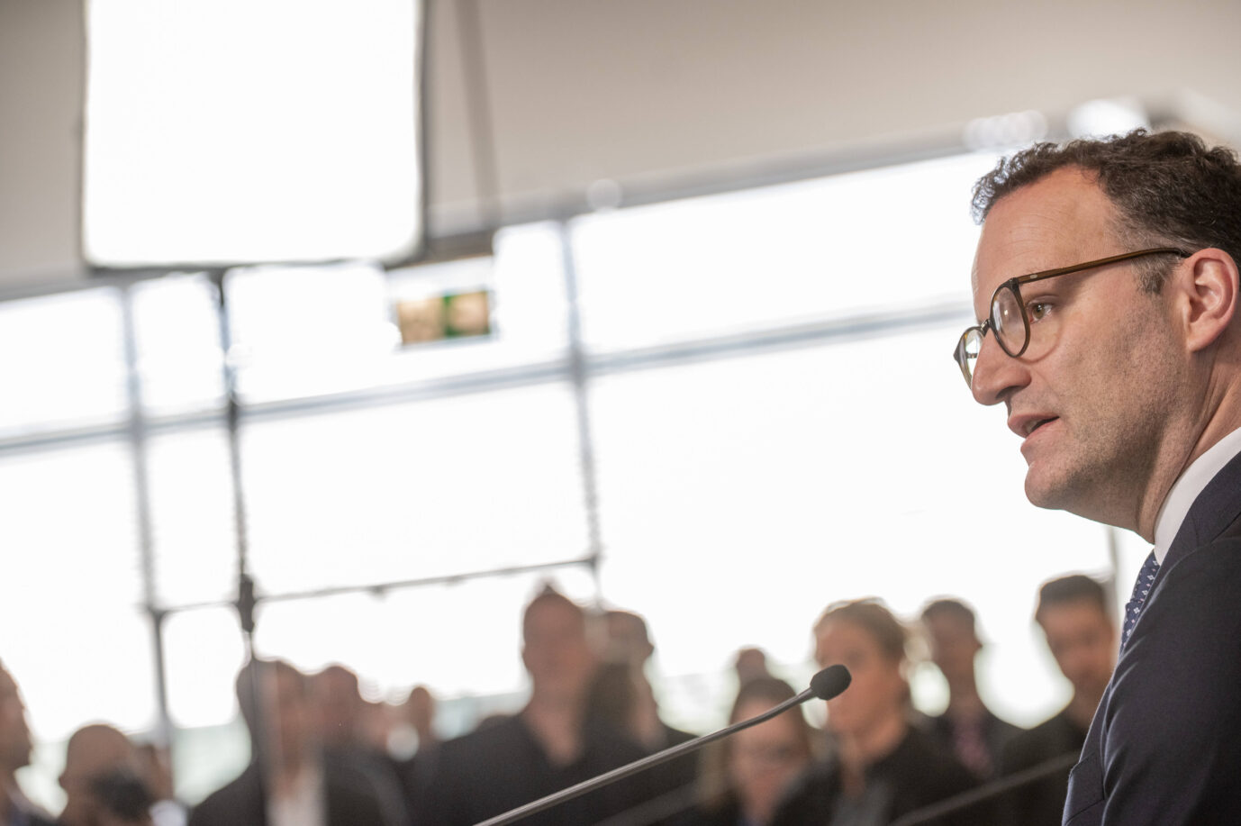 Ein Mann im Anzug mit Brille spricht in ein Mikrofon vor einem unscharfen Publikum in einem hellen, modernen Raum. Die Lichtverhältnisse deuten auf ein professionelles Setting hin, möglicherweise eine Pressekonferenz oder ein öffentlicher Auftritt. Unionsfraktionsführer Jens Spahn will die AfD doch nicht wie eine normale Oppositionspartei behandeln. Foto: IMAGO / Mike Schmidt
