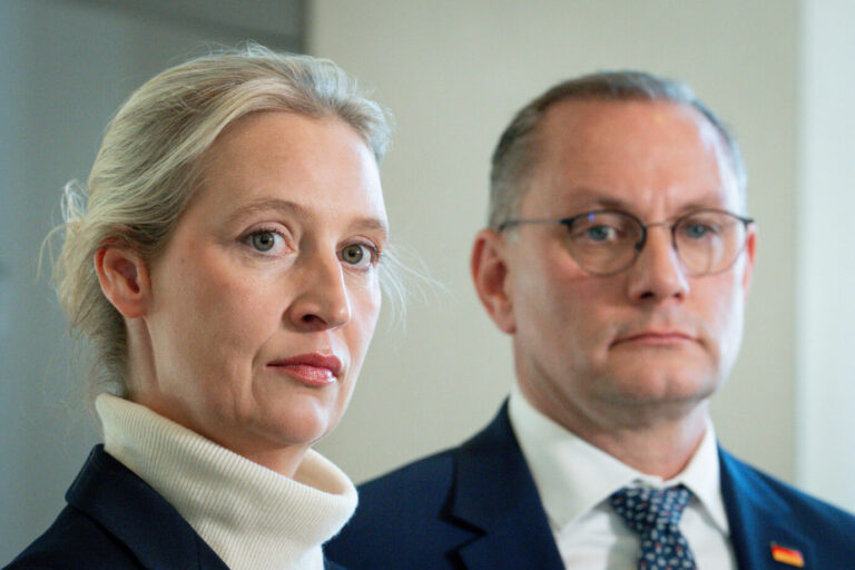 Zwei Personen im Vordergrund, beide in dunkler Kleidung. Links eine blonde Frau mit zurückgebundenen Haaren und hellem Rollkragenpullover, rechts ein Mann mit Brille und Anzug. Beide blicken ernst in Richtung Kamera. Statement der AfD Fraktion im Rahmen der Bundestagssitzung Aktuell, 21.05.2025, Berlin, Dr. Alice Weidel gemeinsam mit Tino Chrupalla bei ihrem Statement zu der Entscheidung des Aeltestenrat im Rahmen der Bundestagssitzung. In der Westlobby des Deutschen Bundestag.