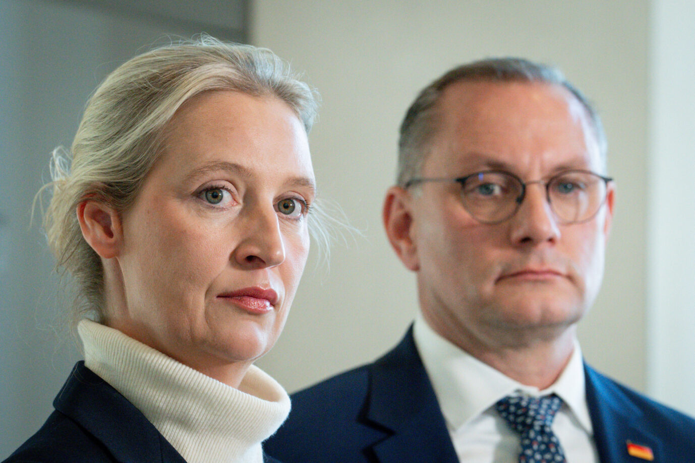 Zwei Personen im Vordergrund, beide in dunkler Kleidung. Links eine blonde Frau mit zurückgebundenen Haaren und hellem Rollkragenpullover, rechts ein Mann mit Brille und Anzug. Beide blicken ernst in Richtung Kamera. Statement der AfD Fraktion im Rahmen der Bundestagssitzung Aktuell, 21.05.2025, Berlin, Dr. Alice Weidel gemeinsam mit Tino Chrupalla bei ihrem Statement zu der Entscheidung des Aeltestenrat im Rahmen der Bundestagssitzung. In der Westlobby des Deutschen Bundestag.