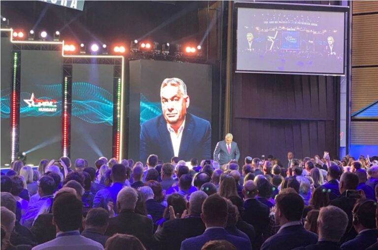 Auf einer Bühne ist groß das Gesicht von Viktor Orban projiziert, davor steht er und spricht - es ist die CPAC 2025 in Budapest