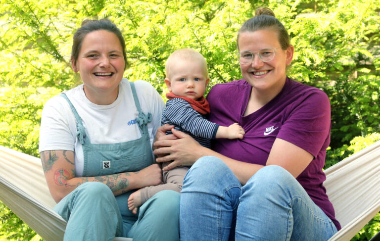 Jana (l-r), der zehn Monate alte Remo und Juliane in ihrem Garten hinter ihrem Haus in Berlin. Vater, Mutter, Kind: Nicht alle Familien passen in dieses Bild. Für Regenbogenfamilien gibt es seit zehn Jahren eine feste Anlaufstelle in Berlin. In Sachen Gleichstellung hat sich für sie schon viel getan - aber es gibt noch Luft nach oben. (zu dpa: Regenbogenfamilie Schnee - zwei Mamas, Kind und Hund)