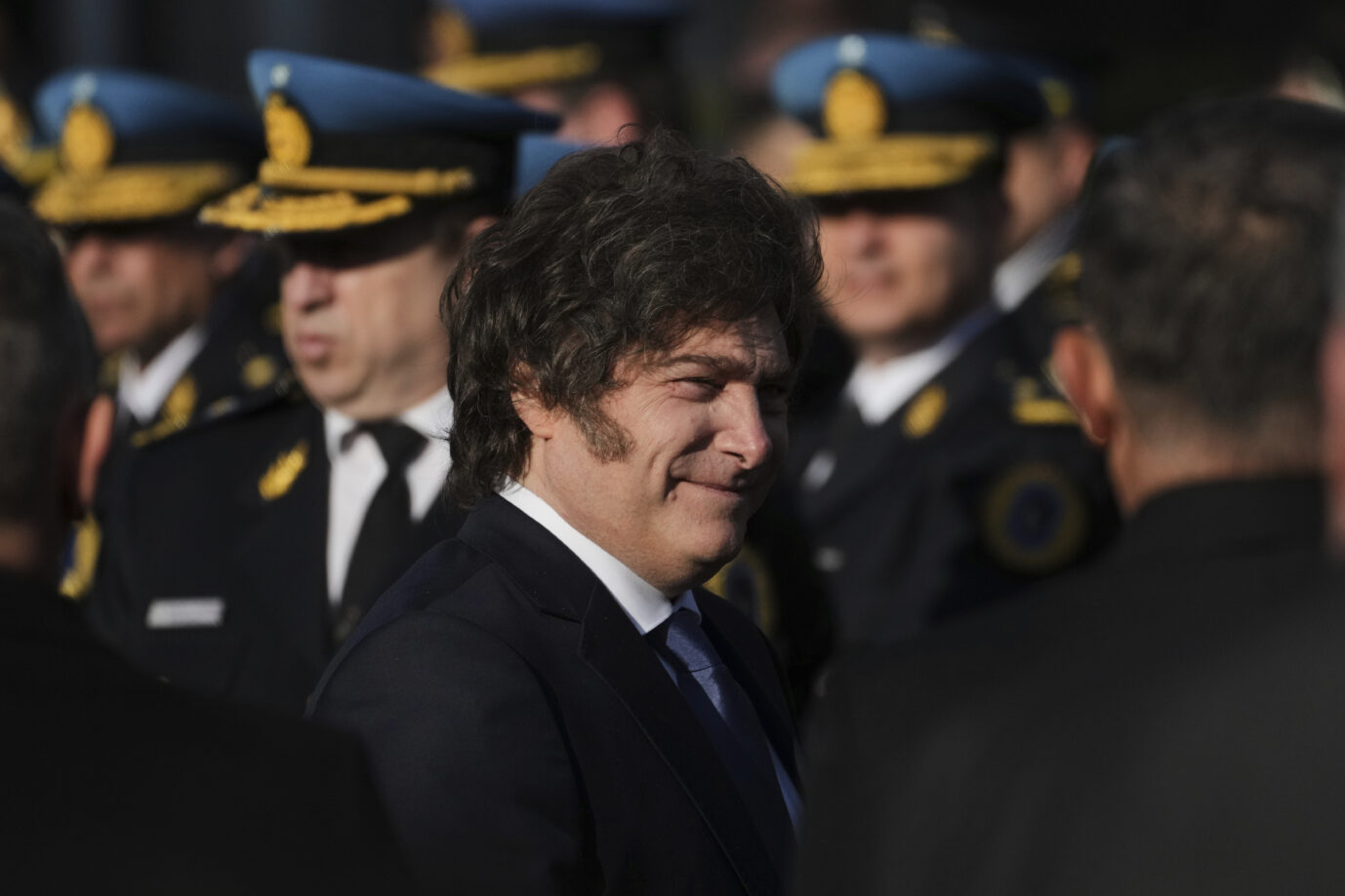 Der argentinische Präsident Javier Milei im Anzug mit blauer Krawatte bei einer offiziellen Veranstaltung, im Hintergrund uniformierte Polizisten mit blauen Schirmmützen und goldenen Abzeichen. Milei blickt leicht zur Seite und lächelt. Die Szene spielt im Freien bei Tageslicht. Argentiniens Präsident Javier Milei umringt von Polizisten: Nach der Enttarnung russischer Agenten will er die Bundespolizei zur Spionageabwehr ausbauen. Foto: picture alliance / ASSOCIATED PRESS | Rodrigo Abd