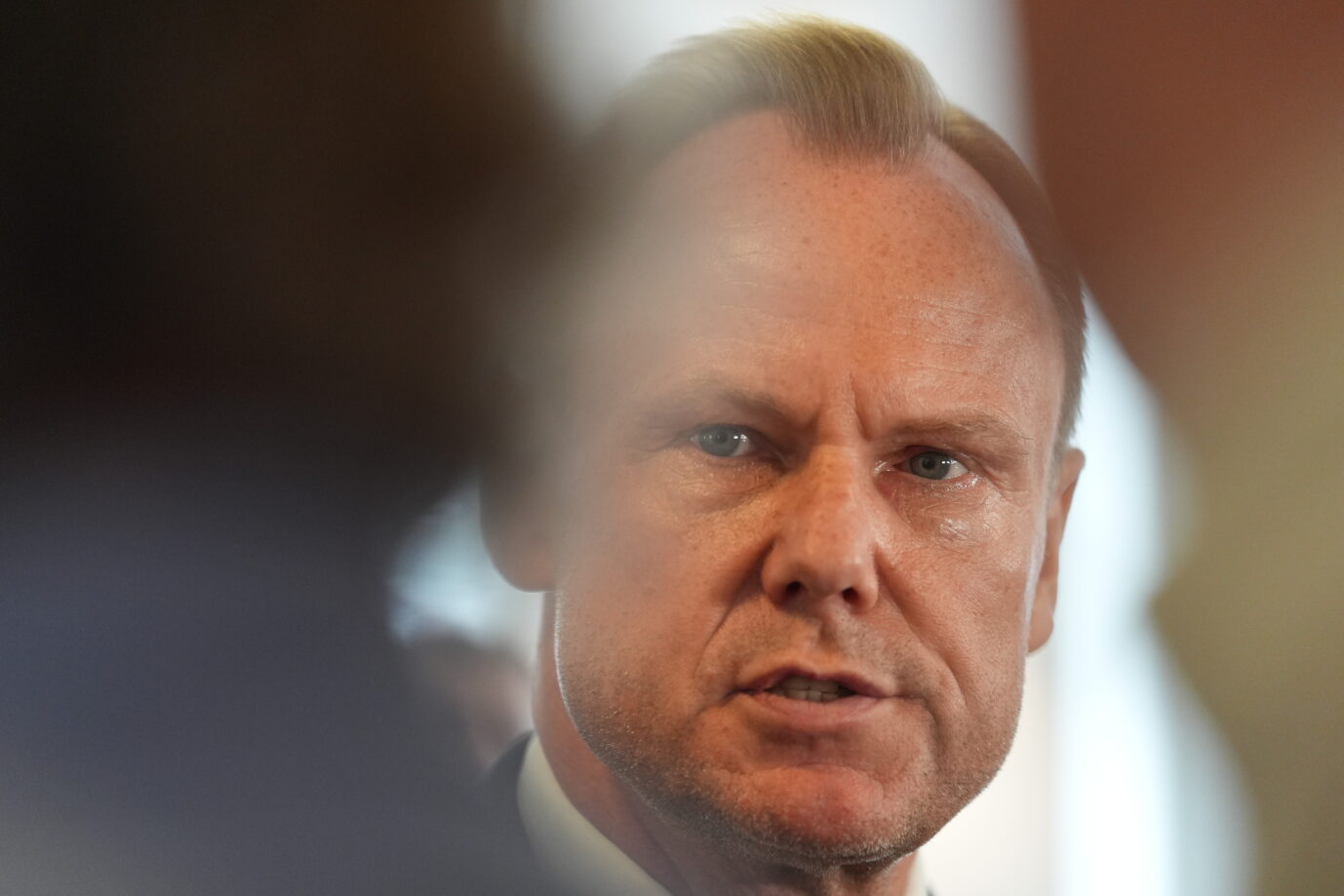 Andy Grote (SPD), Hamburgs Senator für Inneres und Sport, spricht mit ernstem Blick zu Pressevertretern. Der Hintergrund ist unscharf, im Vordergrund dominieren Schatten und verschwommene Silhouetten. Das Bild entstand während einer Stellungnahme zum Angriff auf Polizisten bei einer Festnahme im Stadtpark.