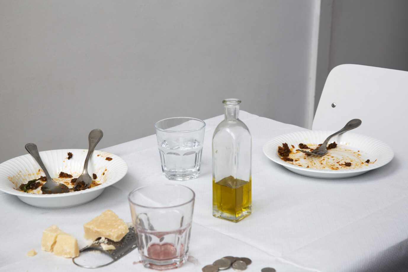 Auf einem Tisch mit weißem Laken sieht Man Teller mit Essensresten, ein angebrochenes Stück Peccorino und eine Karaffe Olivenöl – Symbolbild für Essensgebote und -verbote
