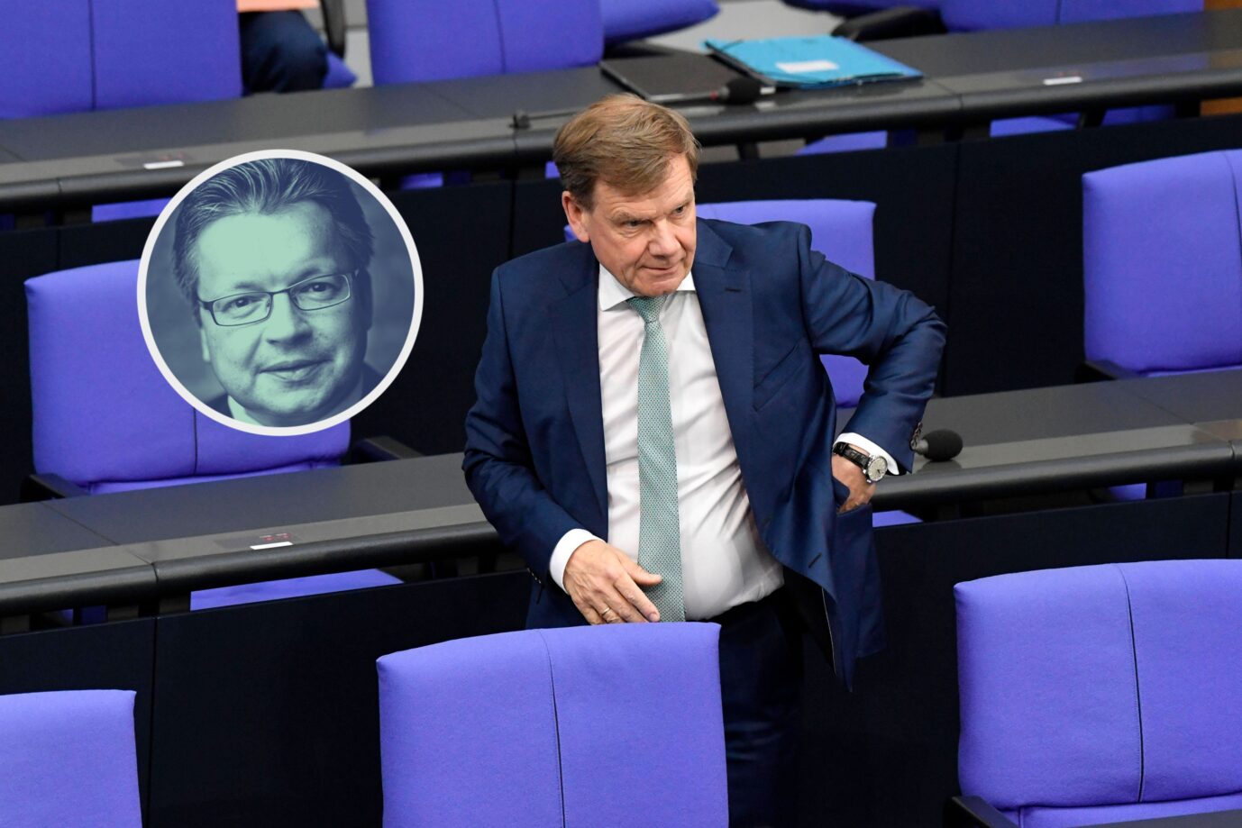 Ein älterer Mann mit lichtbraunen Haaren und dunkelblauem Anzug steht leicht vorgebeugt im Plenarsaal des Deutschen Bundestages zwischen mehreren leeren Sitzen mit auffällig lilafarbener Polsterung. Er trägt ein weißes Hemd und eine hellgrüne Krawatte, seine linke Hand ruht in der Hüfte, die rechte an der Sessellehne. Die Szenerie wirkt angespannt, als befände sich der Mann in einer Wartesituation oder einem Moment der Konzentration. Vor ihm sind mehrere Sitzreihen sichtbar, auf den Tischen liegen Mikrofone, Papiere und Ordner. In der linken oberen Ecke des Bildes ist ein rundes Schwarzweißporträt eines weiteren Mannes eingeblendet: Er trägt Brille, hat kurzes, nach hinten gekämmtes Haar und blickt frontal in die Kamera. Das Porträt wirkt wie ein Kommentar- oder Autorenhinweis. Außenminister Johann Wadephul auf der Regierungsbank im Bundestag: Der Christdemokrat kapituliert vor den Grünen. Foto: IMAGO / Future Image