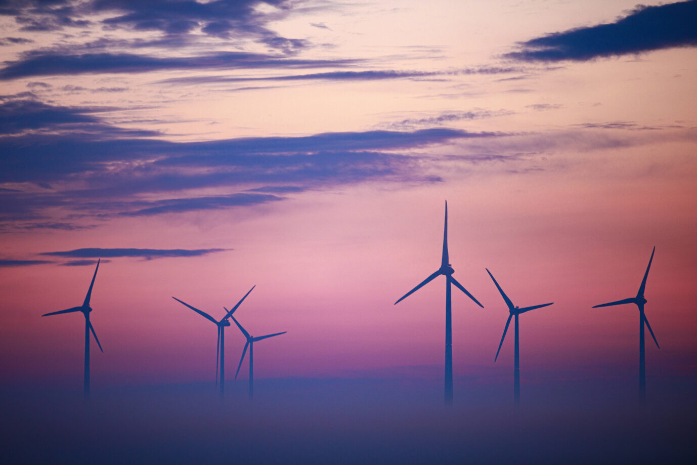 In einer dunstigen Abenddämmerung sind mehrere Windräder zu sehen – Symbolbild für die Energiewende in Deutschland