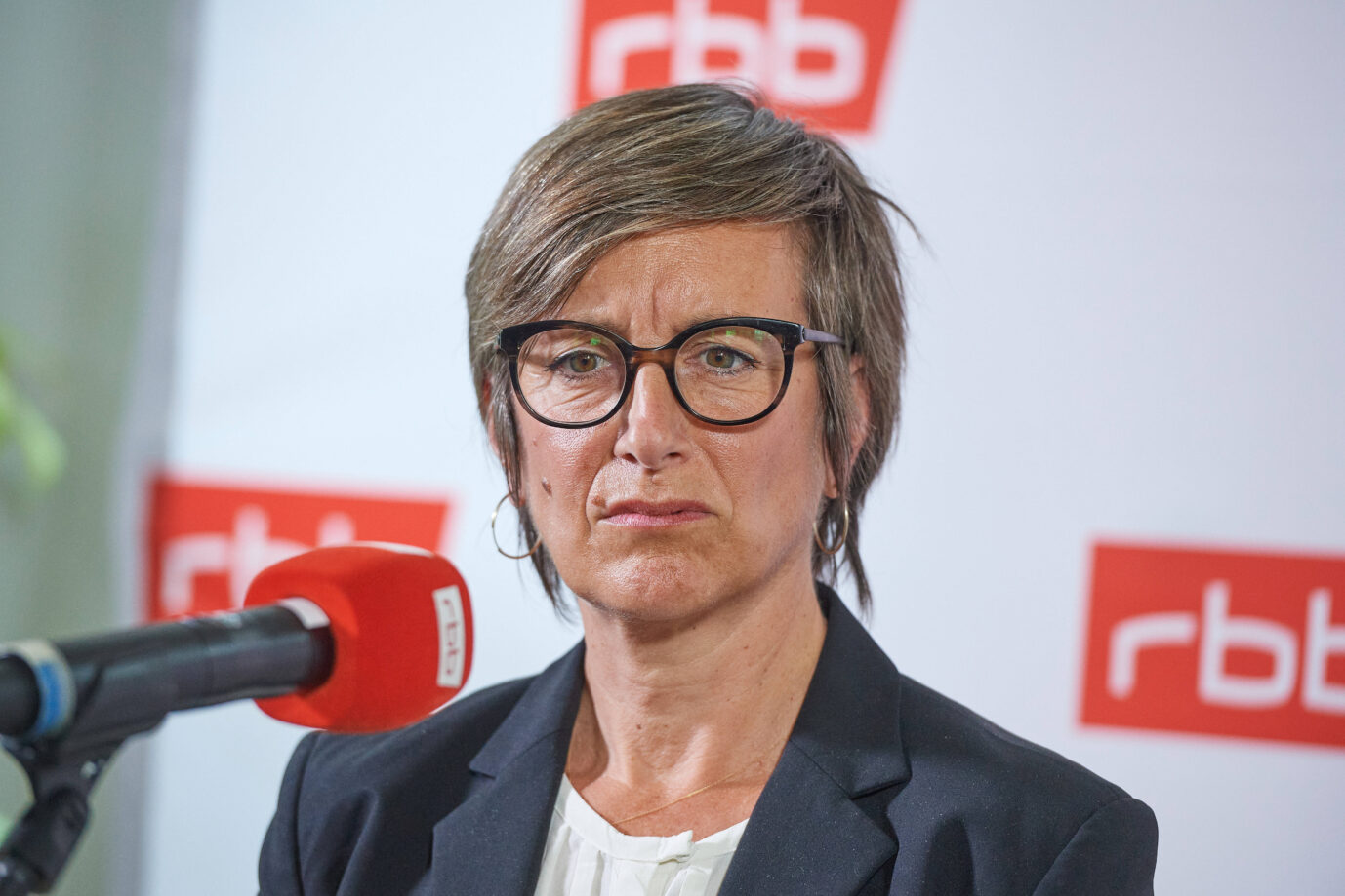 Vor einem weißen Hintergrund mir RBB-Logo steht die Journalistin und RBB-Chefin Ulrike Demmer und schaut mürrisch – noch immer gibt der Sender horrende Summen für ehemalige Mitarbeiter aus