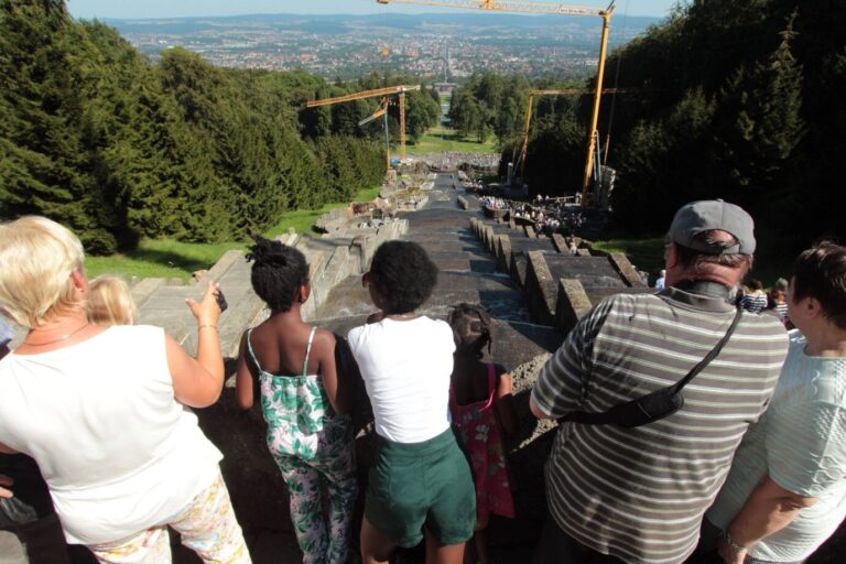 Eine Gruppe Menschen steht vor einem Wasserspiel und schaut in ein Tal herab – es handelt sich um den Schloßpark in Kassel, offiziell die zufriedenste Stadt Deutschlands