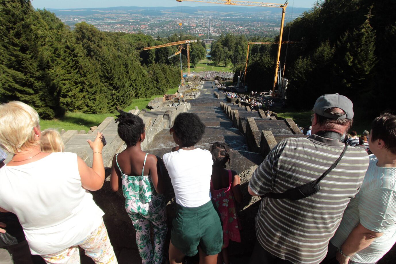 Eine Gruppe Menschen steht vor einem Wasserspiel und schaut in ein Tal herab – es handelt sich um den Schloßpark in Kassel, offiziell die zufriedenste Stadt Deutschlands